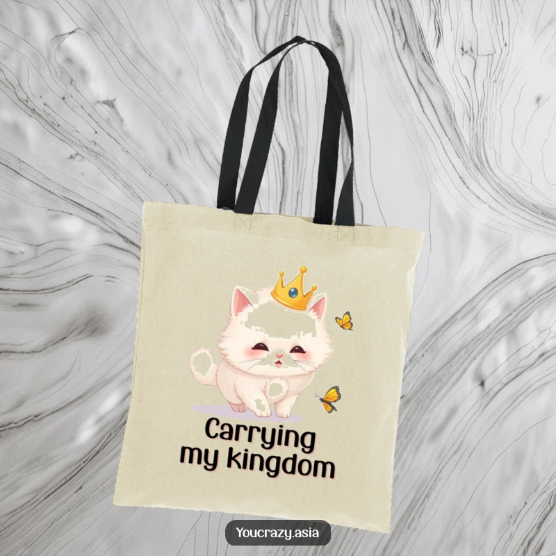 Funny tote bag showcasing a fluffy white cat in a golden crown, comically chasing a butterfly, perfect for stylish, humorous shoppers.